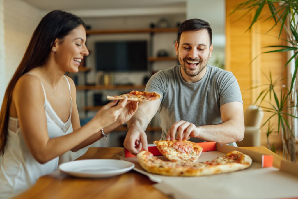 Happy man and woman enjoying pizza for a cheat meal during a diet